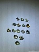 Group of fifteen faceted round gemstones in varied light yellow-green and champagne tones on white background