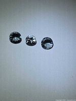 Three loose round faceted gemstones on neutral background