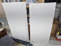 Front view of two identical white pegboard panels leaning against shelving
