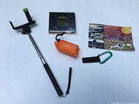 All items laid out: selfie stick, black document holder, orange bag pouch, information card, carabiner strap