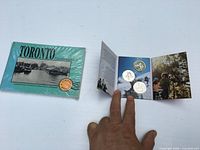Front view of sealed postcard book and opened Canadian Tire coin folder with three coins