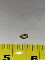 Top view of faceted pear-cut citrine against tape measure indicating approx 10 mm length