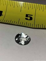 Top view of oval faceted white topaz beside tape measure showing size under 1 cm