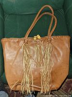 Front view of brown leather shoulder bag showing braided handles and long leather tassels