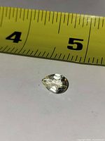 Top view of pear-shaped white topaz beside measuring tape showing approx 12 mm length
