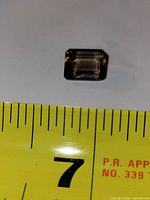 Top view of rectangular step-cut light amethyst next to tape showing roughly 10 mm width