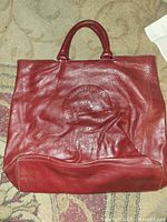 Front view showing red leather body, embossed logo, handles
