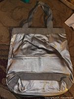 Front view of metallic silver DKNY tote showing exterior pocket and webbing handles