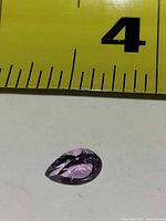 Pear-shaped faceted amethyst beside ruler showing scale