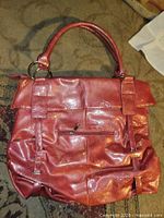 Front view of glossy pink handbag with handles, zip pocket and buckle accents