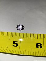Top view of oval faceted amethyst next to measuring tape showing size just under 1 cm