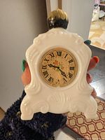 Front view showing rococo porcelain clock perfume bottle with Roman numeral face and crazing