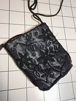 Full view of black satin evening bag with braided strap and floral bead design