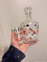 Decanter with stopper beside one shot glass, showing card suit graphics and checker band