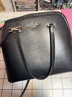 Front view of black pebbled leather Kate Spade crossbody bag showing logo, strap, zipper