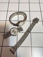 Two wristwatches and separate metal mesh band on grid background
