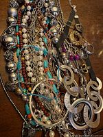 Overview of piled necklaces and bracelets showing beads, chains and large circle pendant
