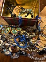 Overview of jewelry spilling from tin, showing bracelets and beaded necklaces