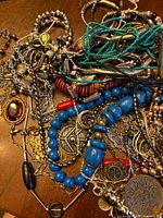 Overall view of tangled jewelry pile showing blue beads, turquoise strands, metallic pieces