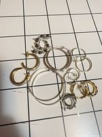 Overview of eight pairs hoop earrings assorted sizes and metal tones