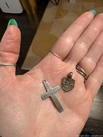 Hand holding cross and shield pendants front view