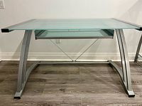 Front view of glass-top metal desk with keyboard tray visible