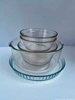 Nested clear glass mixing bowls stacked inside large bowl on top of fluted glass flan dish