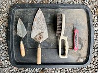 Four masonry tools on tray: two trowels, wire brush, utility knife
