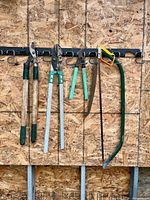 Five garden cutting tools hanging: two long loppers, hedge shears, medium loppers, bow saw