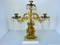 Front view of gilt metal three-arm candelabrum with crystal prisms on marble base