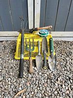 All eight items arranged on gravel: basket, five hand tools, hand hoe, wire spool