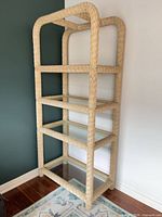 Full view of wicker rattan bookcase showing four glass shelves and overall structure