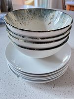 Stack of four speckled-rim bowls on five white plates
