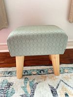 Side view of seafoam green fabric footstool on wooden legs