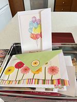 Assorted cards inside red tin; balloon birthday card and floral card visible