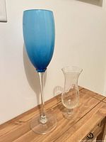 Blue gradient stemmed vase beside clear vase on wooden surface