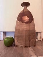 Front view of tall stoneware vase beside apple for scale