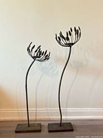 Two wrought iron candle holders of differing heights on square bases against wall