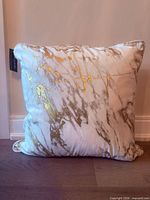 Front view of square cream velvet pillow with gold pattern and Tahari tag
