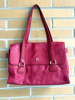 Front view of red Etienne Aigner purse hanging on brick wall