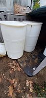 Two white plastic 55-gallon barrels standing upright beside shed