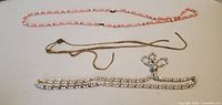 Three necklaces laid flat: pink bead, gold-tone chain, rhinestone bow