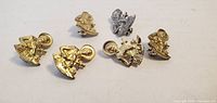 Six religious figure lapel pins, five gold-tone, one silver-tone, front view with clasps visible