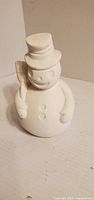 Front view of unpainted ceramic snowman showing buttons, hat, broom