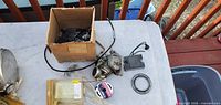 Overview of lot: box of hardware, carburetor assembly, finned head, retaining ring, wire spool, plastic case on table