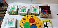 Overall lot showing 4 clock dial boxes, teaching clock, tin with math rods, flash card pack