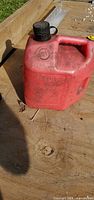 Front view of red plastic gasoline can showing handle, cap, vent button, embossed lettering