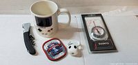 All five items laid out: compass package, mug, corkscrew, patch, figurine