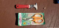 Top view of red scraper and packaged orange scissors on tabletop