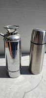 metal fire extinguisher and stainless thermos side by side front view
